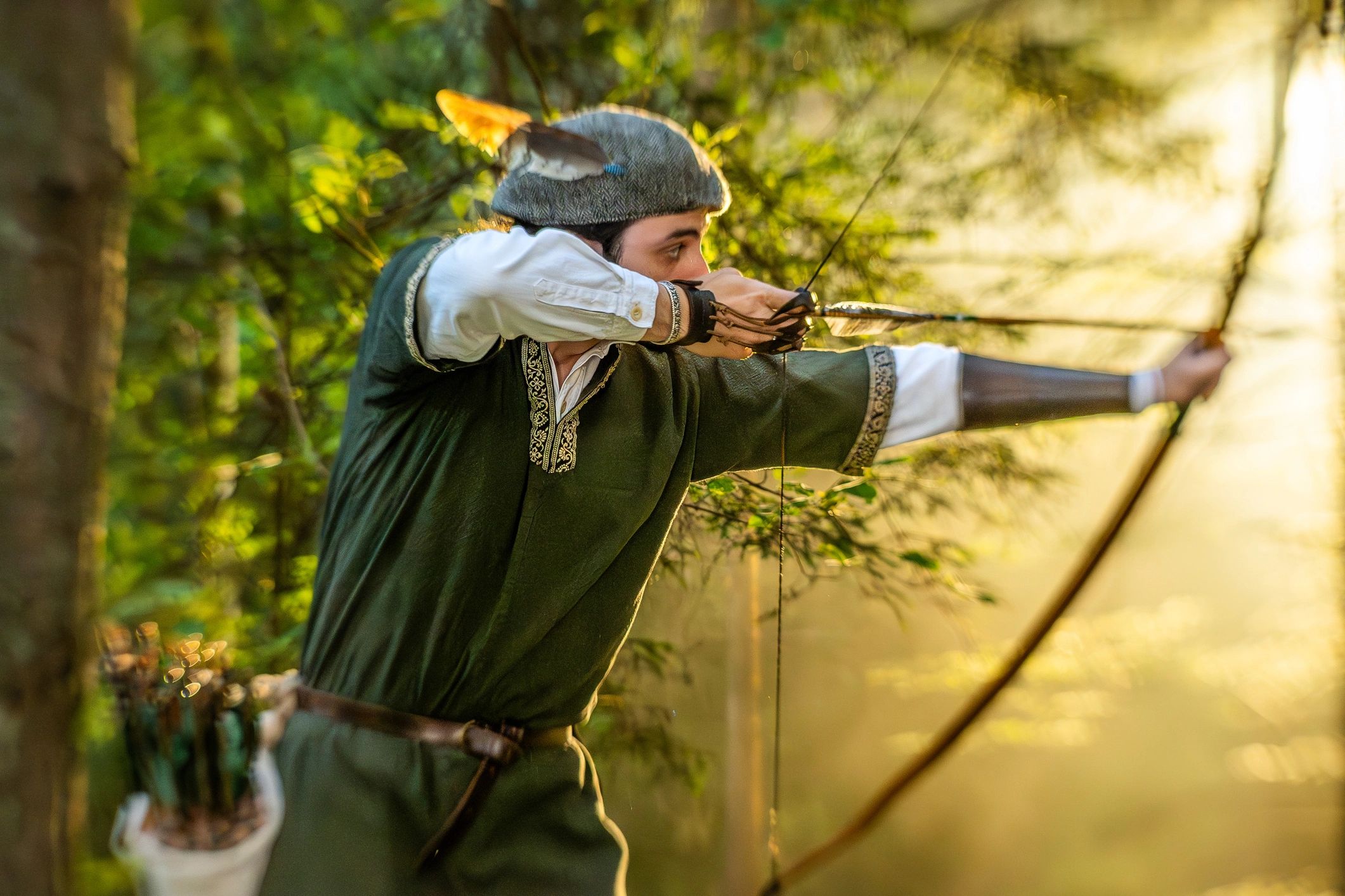 Archer in medieval attire aiming longbow in forest