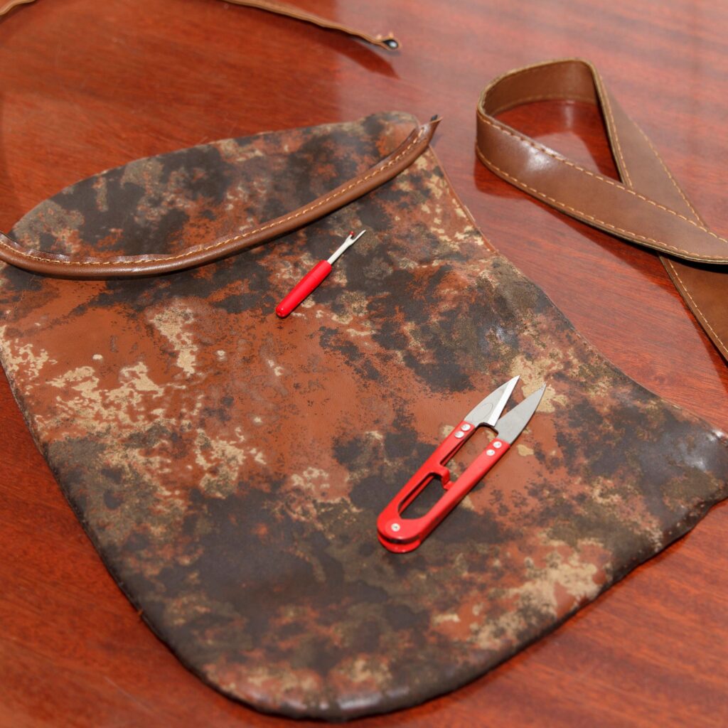 Repair project with a worn brown purse, seam ripper, and thread snips on a wood surface.